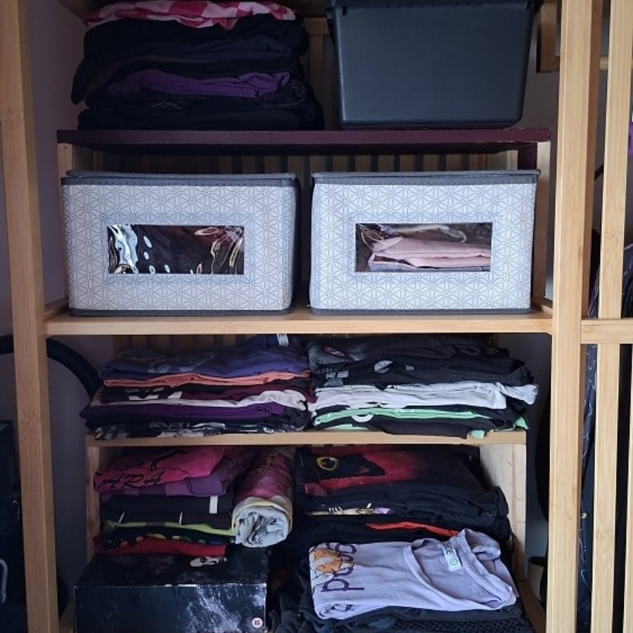 Open wardrobe shelf with two patterned fabric boxes and folded clothes on shelves below.