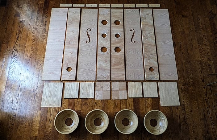 speaker parts - IKEA Hackers Light wooden speaker enclosure pieces arranged on a wooden floor, long planks with circular holes and two carved'S' shapes; four round bowls sit along the front.